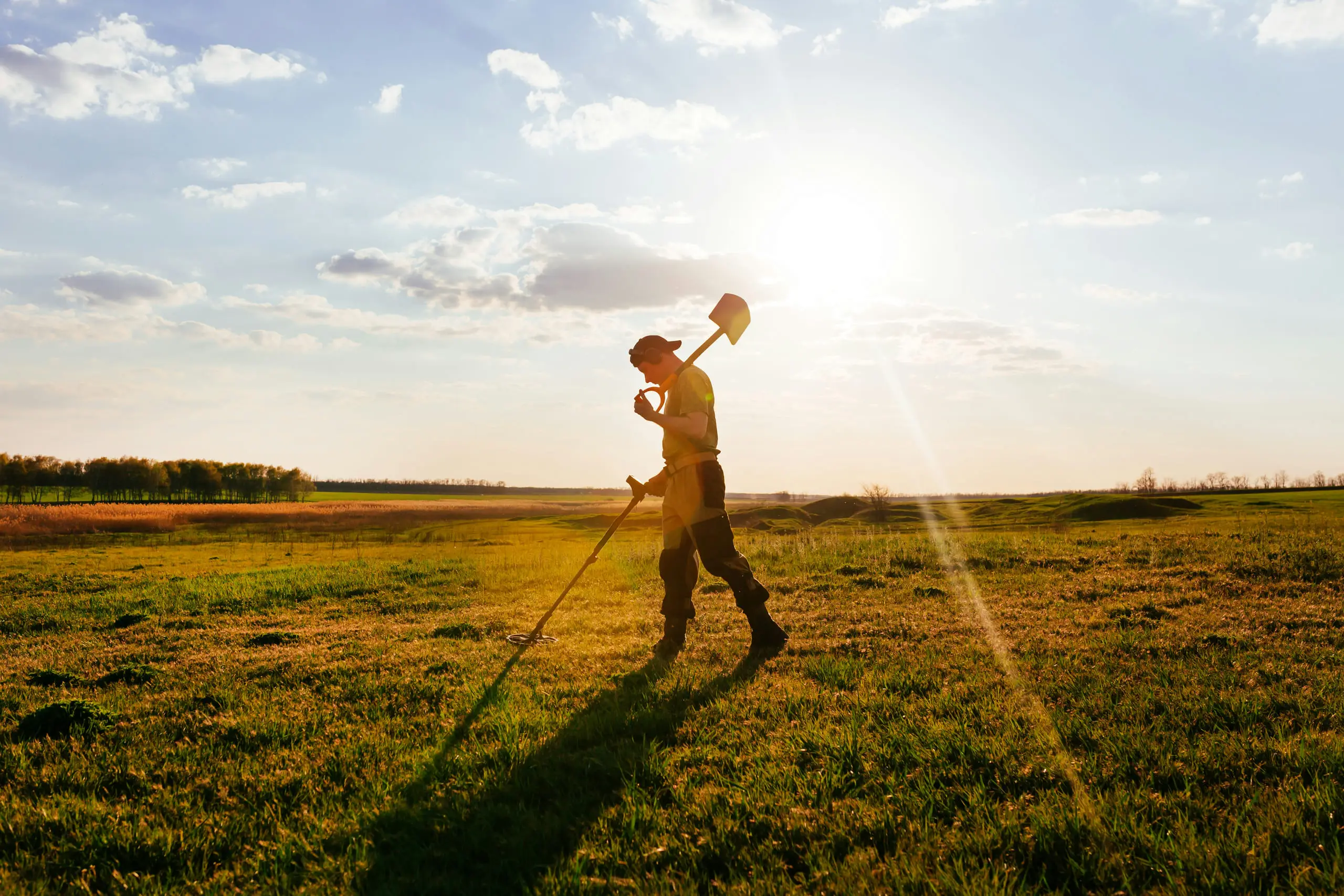 Prospector scanning open grassland with a metal detector at sunset